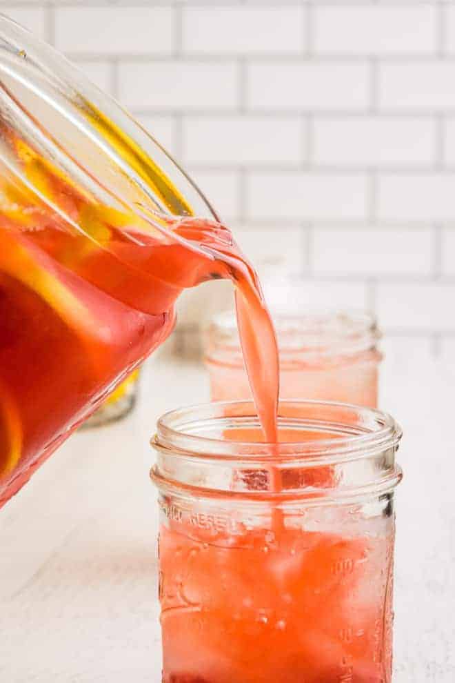 Pink lemonade being poured from a pitcher into a mason jar.