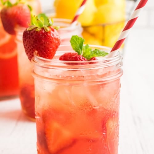 Sparkling berry pink lemonade in a mason jar with a red and white straw. Garnished with a strawberry and fresh mint.