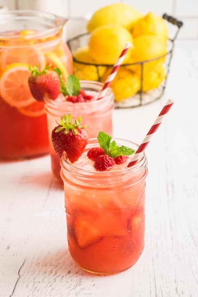 Light red drink in glasses with red and white striped paper straws.