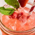 Close up view of a pink lemonade on ice, garnished with berries and fresh mint.