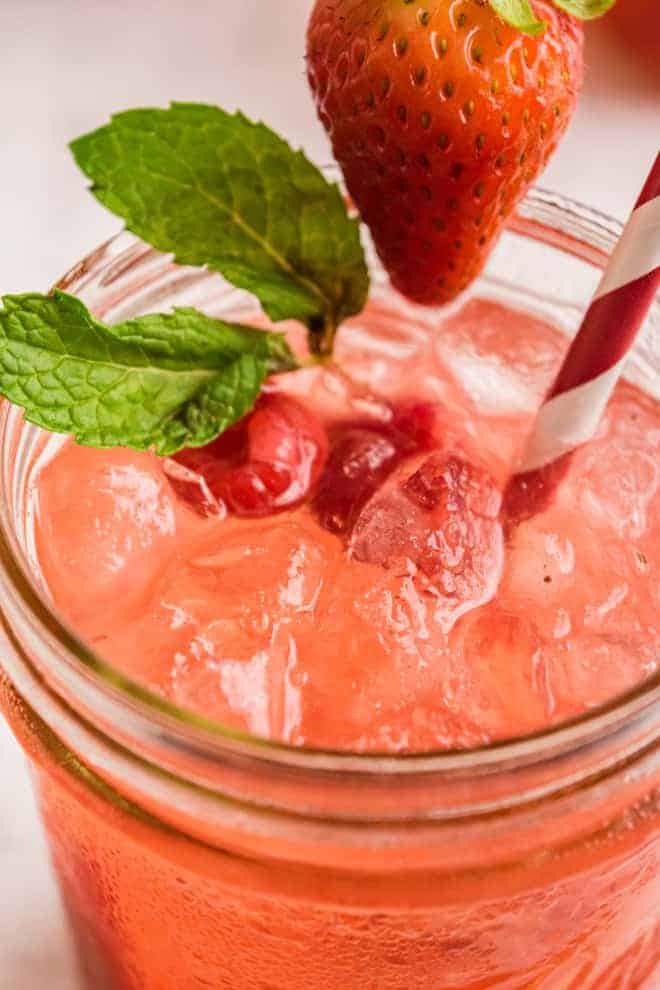 Close up view of a pink lemonade on ice, garnished with berries and fresh mint.