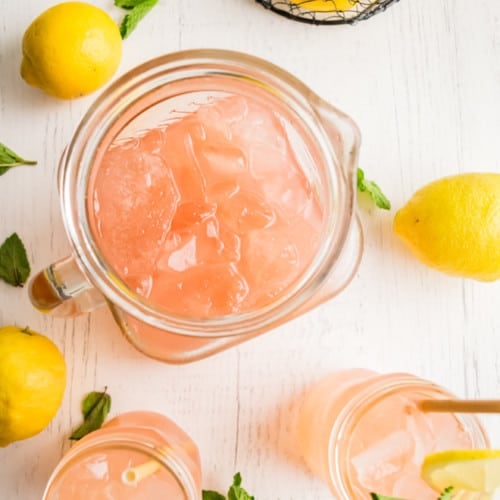 Overhead view of a pitcher and two glasses of a pink beverage on ice.