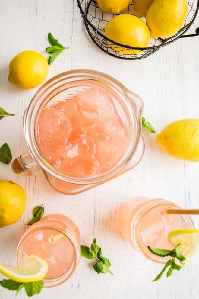 Overhead view of a pitcher and two glasses of a pink beverage on ice.