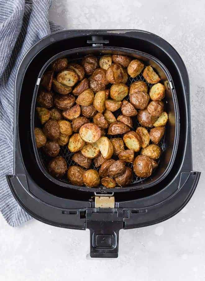 Overhead view of cooked potatoes in a black air fryer on a grey background.