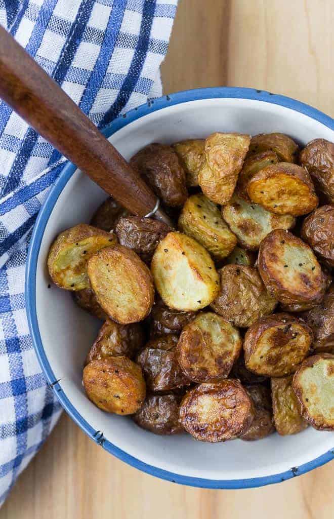 Overhead view of crispy roasted potatoes that have been cooked in an air fryer. They are in a white and blue bowl on a wooden background.