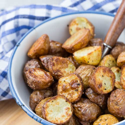 Crispy potatoes in a blue-rimmed white bowl, with a spoon in the bowl.