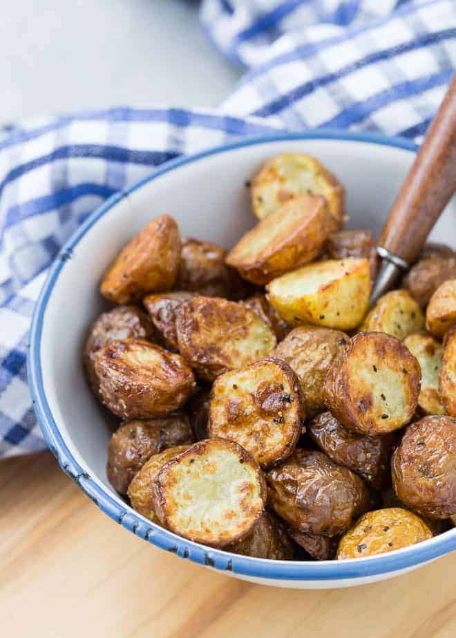 Crispy potatoes in a blue-rimmed white bowl, with a spoon in the bowl.