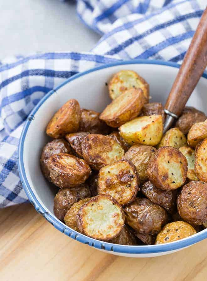 Air fried potatoes in a blue-rimmed white bowl, on a wooden background.