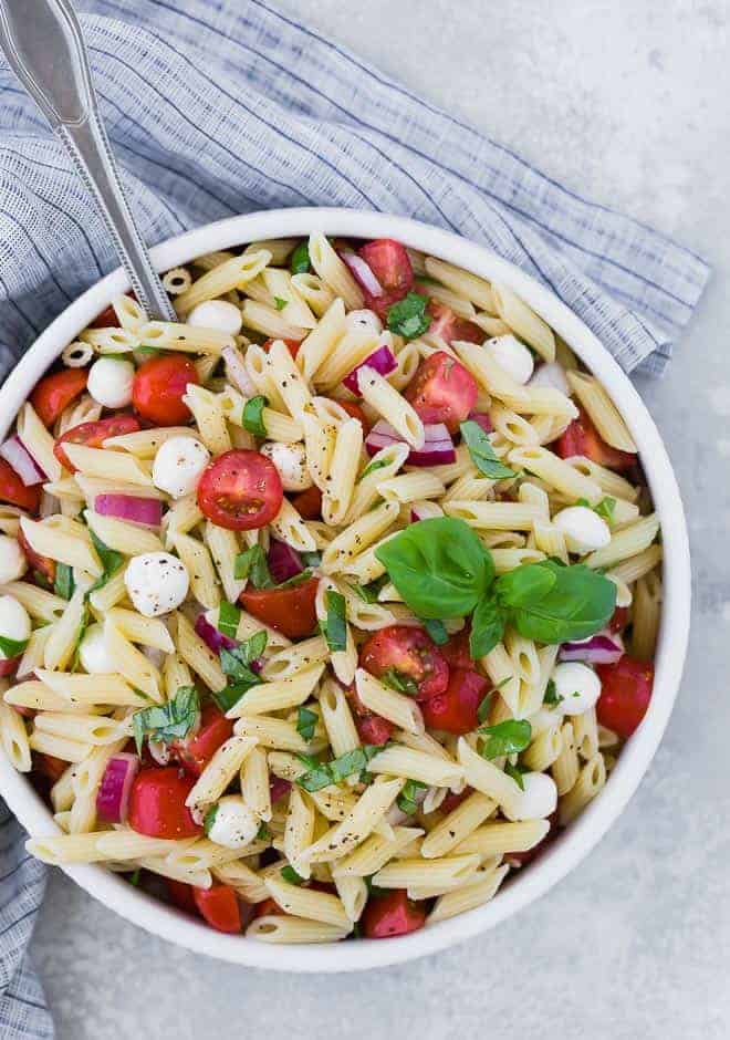 Overhead view of a bowl of pasta salad with tomatoes, fresh mozzarella, red onion, and fresh basil.