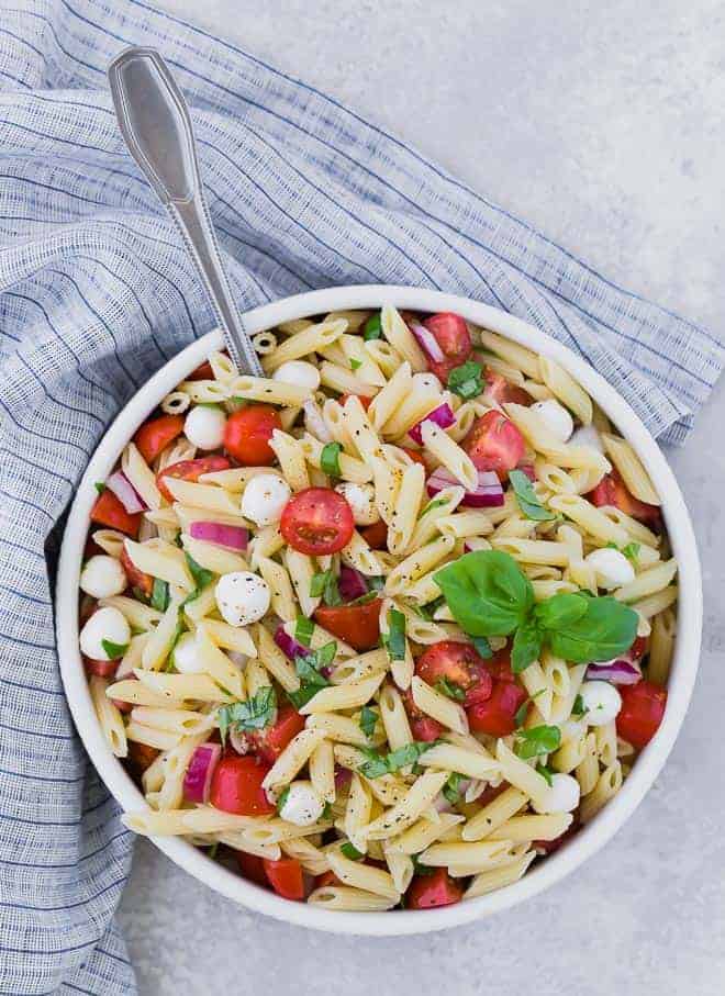 Overhead view of a bowl of pasta salad with tomatoes, fresh mozzarella, red onion, and fresh basil.