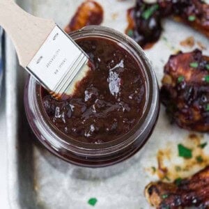 Overhead view of a jar of dark red cherry bbq sauce made with chipotle chiles. A wooden handled brush is inserted into the jar of sauce.