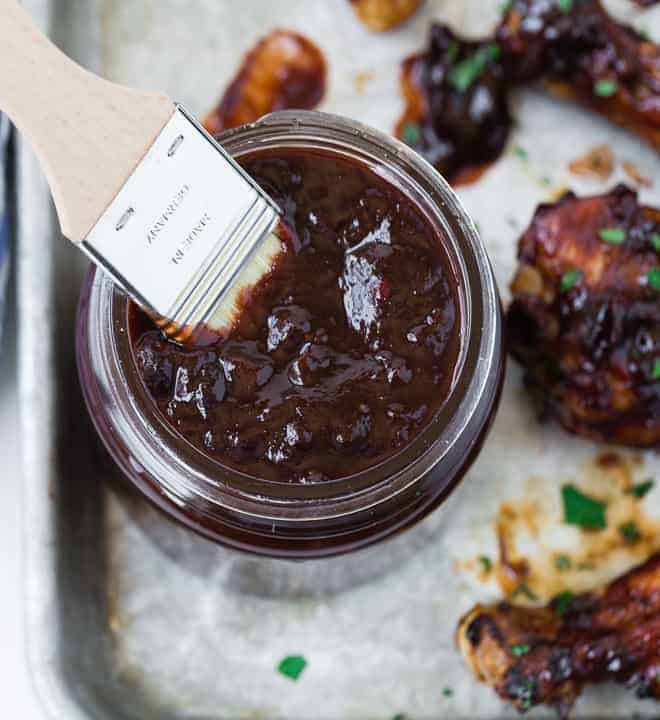 Overhead view of a jar of dark red cherry bbq sauce made with chipotle chiles. A wooden handled brush is inserted into the jar of sauce.