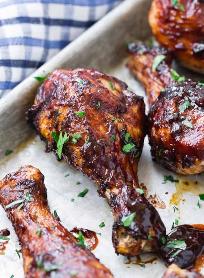 Close up image of a barbecued drumstick, sprinkled with fresh green herbs. It is on a sheet pan with additional chicken drumsticks.