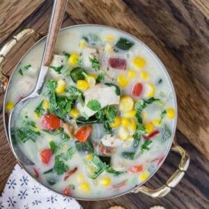 Close up overhead view of chicken corn chowder, in a two-handled bowl, with a spoon.