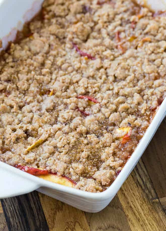 A crumble made with peaches in a white baking dish.