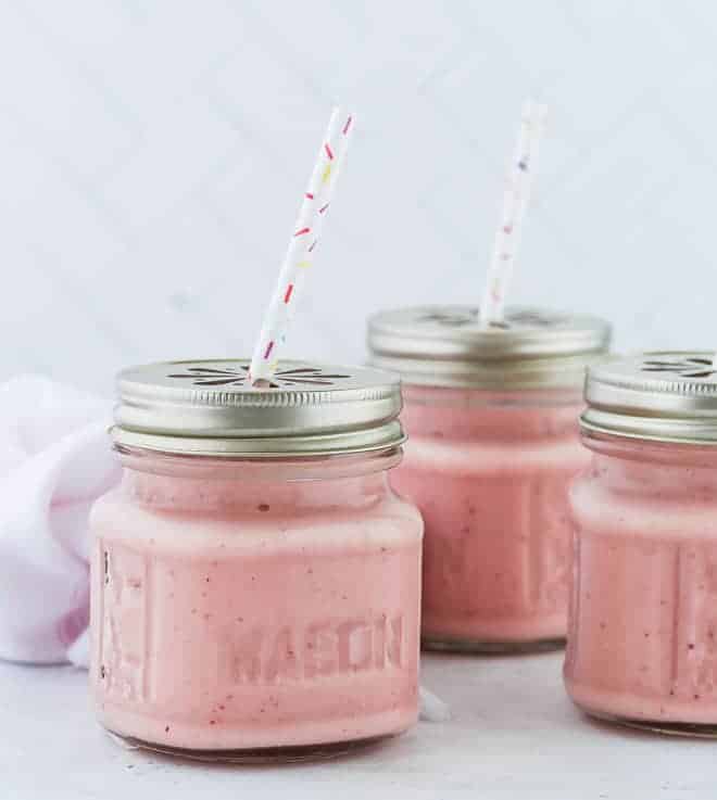 Three pink smoothies in small glass jars. 