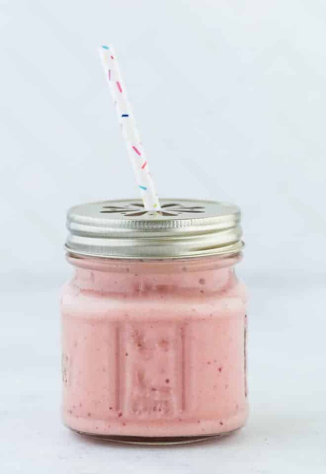 Tropical smoothie, light pink in color, in a small glass jar with a straw. 