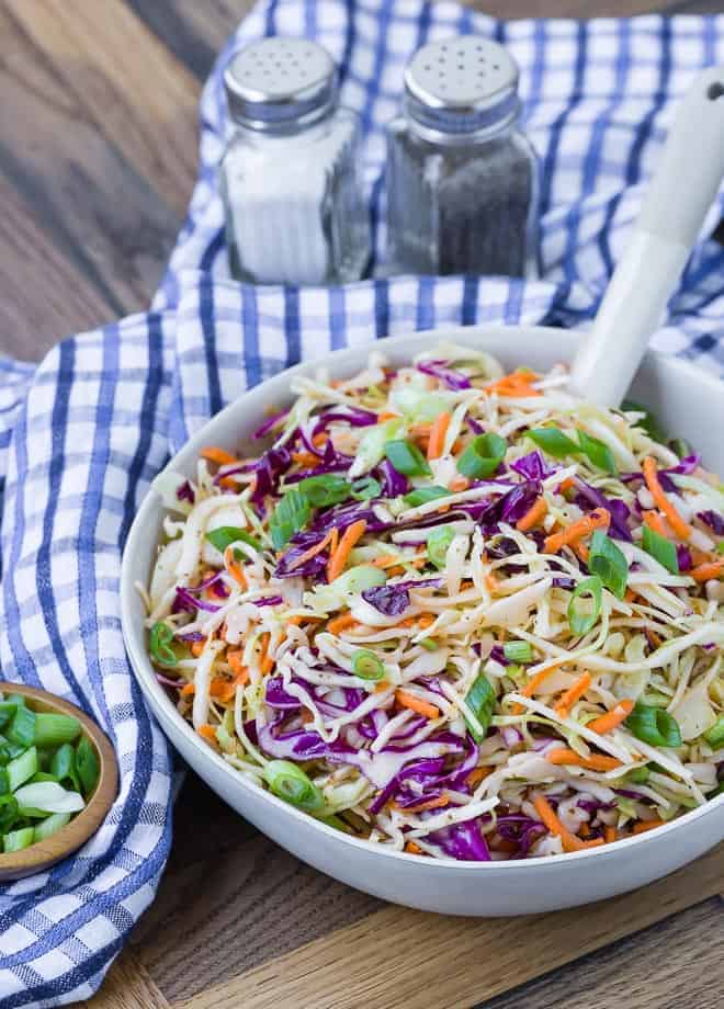 Shredded green and red cabbage, and carrots, in a white serving bowl. Salt and pepper shakers are visible in the background.