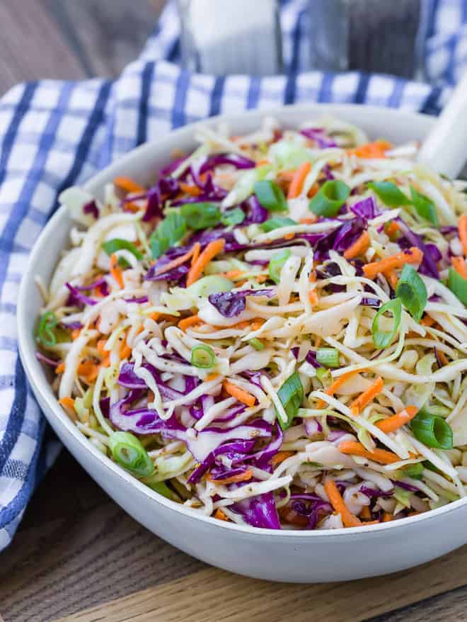 Shredded green and red cabbage, and carrots, in a white serving bowl. Salt and pepper shakers are visible in the background.