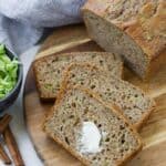 Sliced zucchini bread on a wooden surface. The top slice has a dab of butter on it.