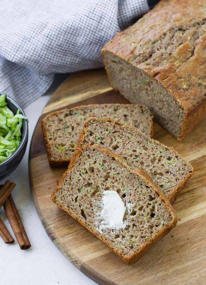 Sliced zucchini bread on a wooden surface. The top slice has a dab of butter on it.