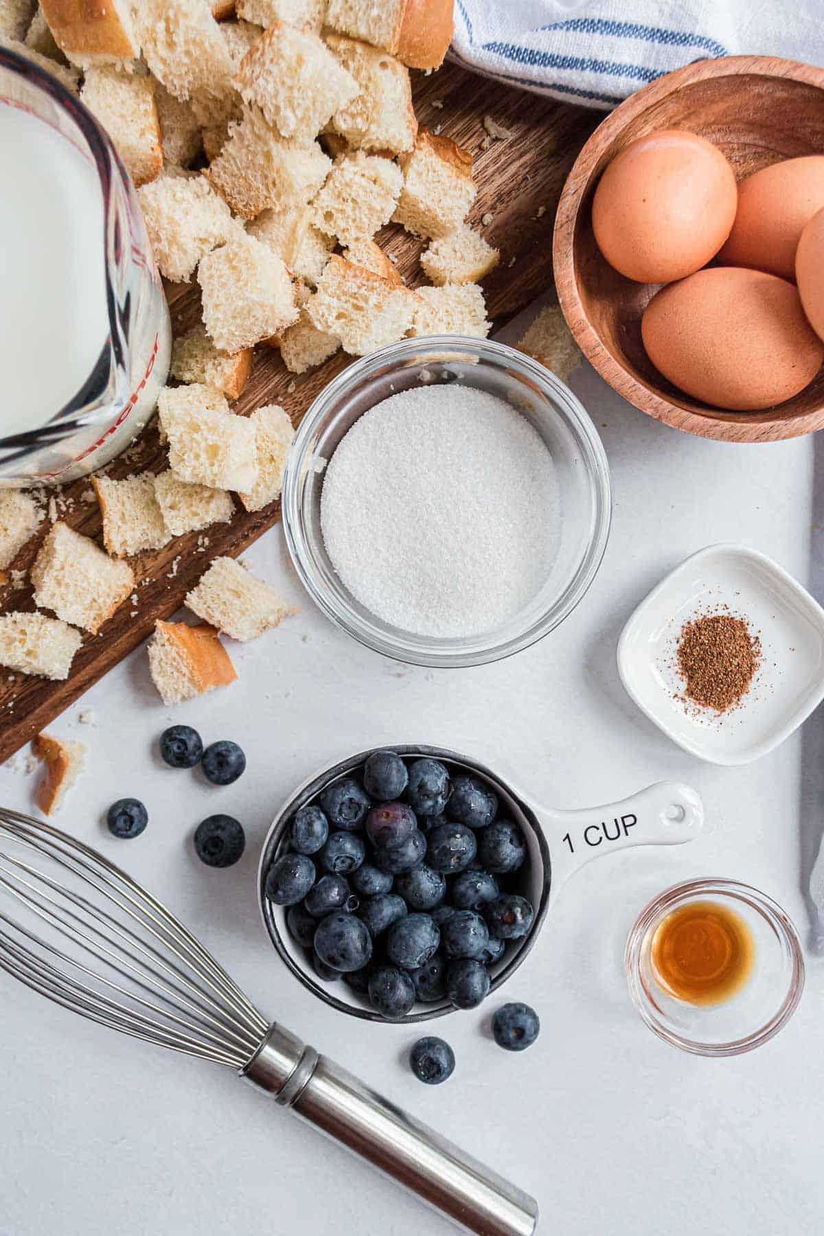 Overhead view of ingredients: cinnamon, cubed bread, milk, eggs, blueberries.