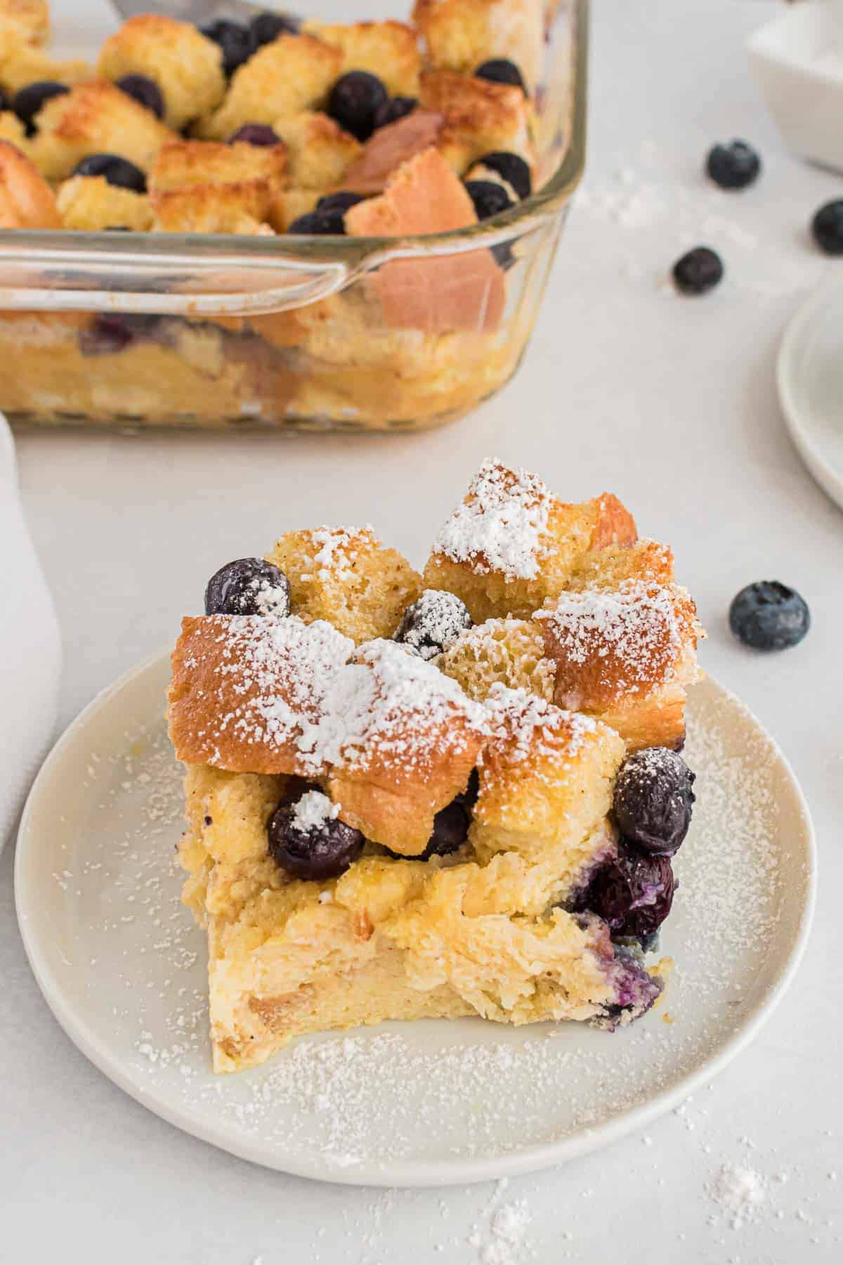 A slice of sugar-dusted bread pudding on a round white plate.