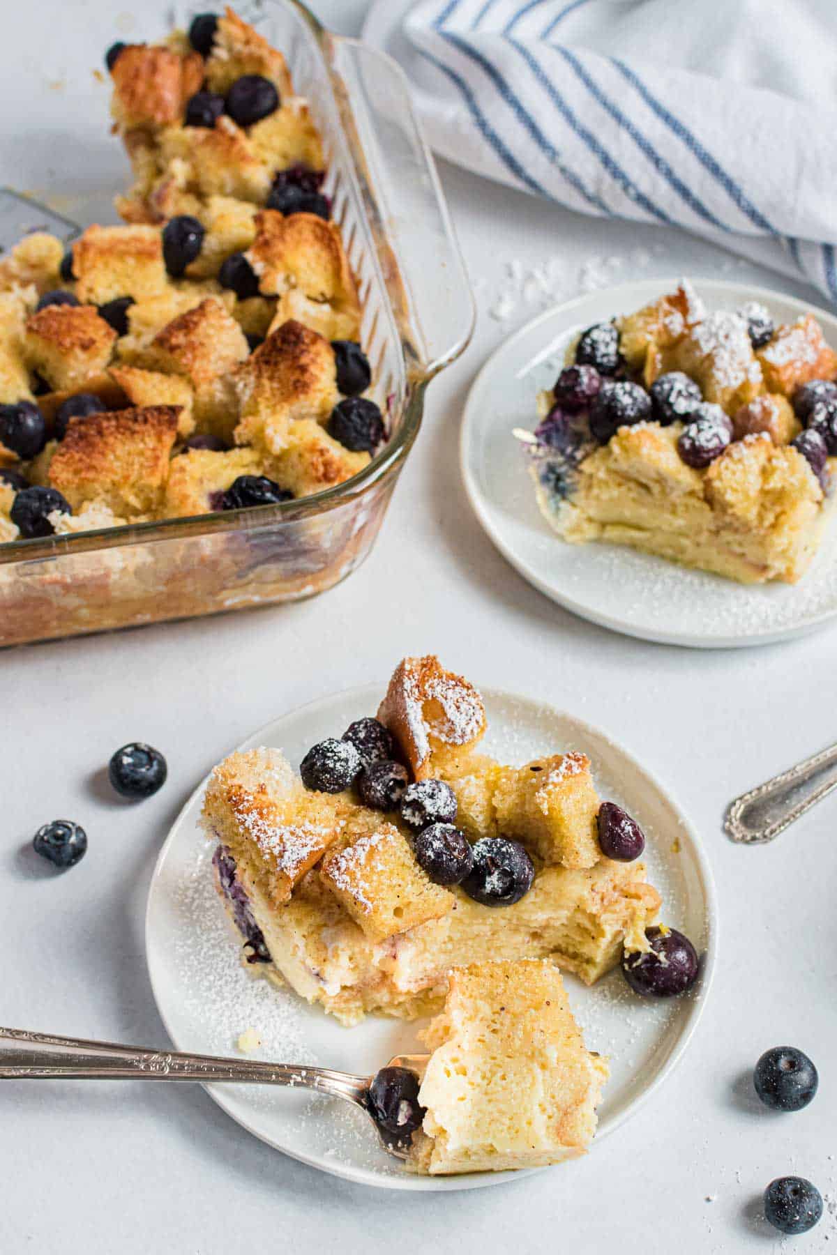 Bread pudding with blueberries on a plate, a fork removing a piece.