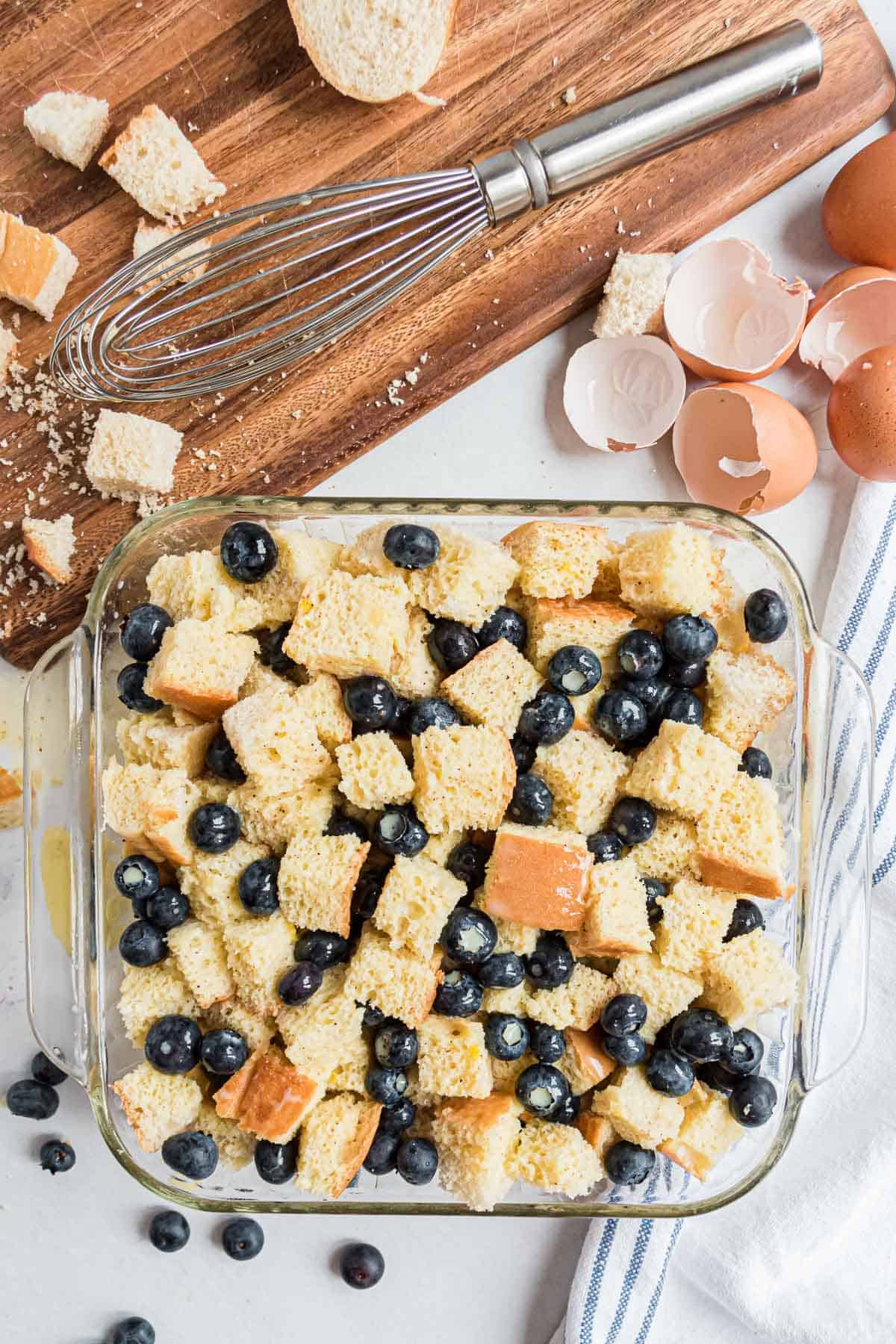 Overhead view of ingredients: cinnamon, cubed bread, milk, eggs, blueberries.