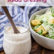 A jar of caesar salad dressing in front of a tossed salad. A text overlay reads "healthy caesar salad dressing."