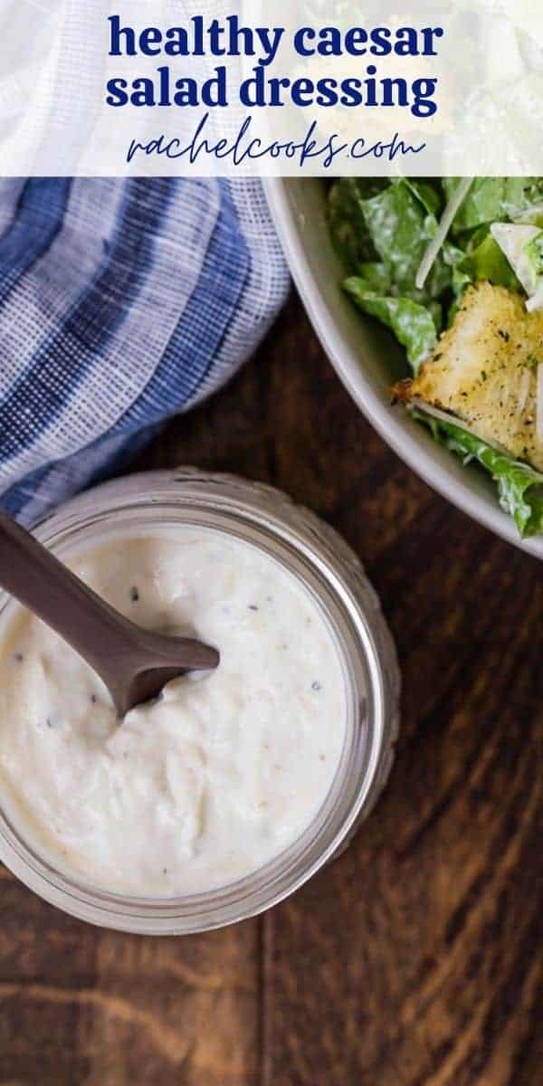 A jar of caesar salad dressing in front of a tossed salad. A text overlay reads "healthy caesar salad dressing."