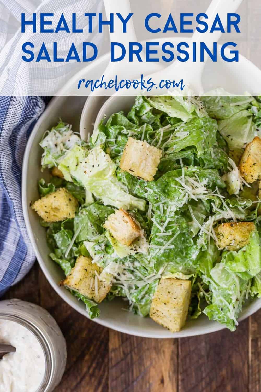 A jar of caesar salad dressing in front of a tossed salad. A text overlay reads "healthy caesar salad dressing."