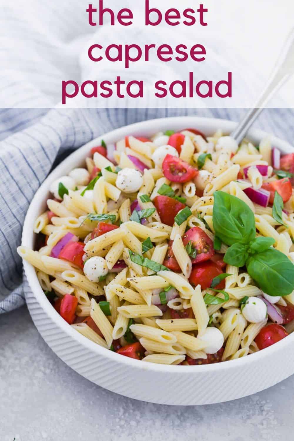 A white bowl full of pasta, fresh mozzarella, tomatoes, and fresh basil. A text overlay reads "the best caprese pasta salad."