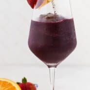 Tall stemmed glass of a dark red frozen beverage. Text overlay reads "frozen sangria."