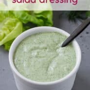 Green and white salad dressing in a white bowl with a black spoon. Text overlay reads "green goddess salad dressing."