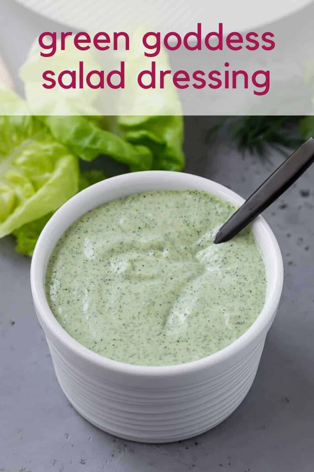 Green and white salad dressing in a white bowl with a black spoon. Text overlay reads "green goddess salad dressing."