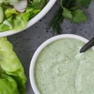 Green and white salad dressing in a white bowl with a black spoon. Text overlay reads "green goddess salad dressing."