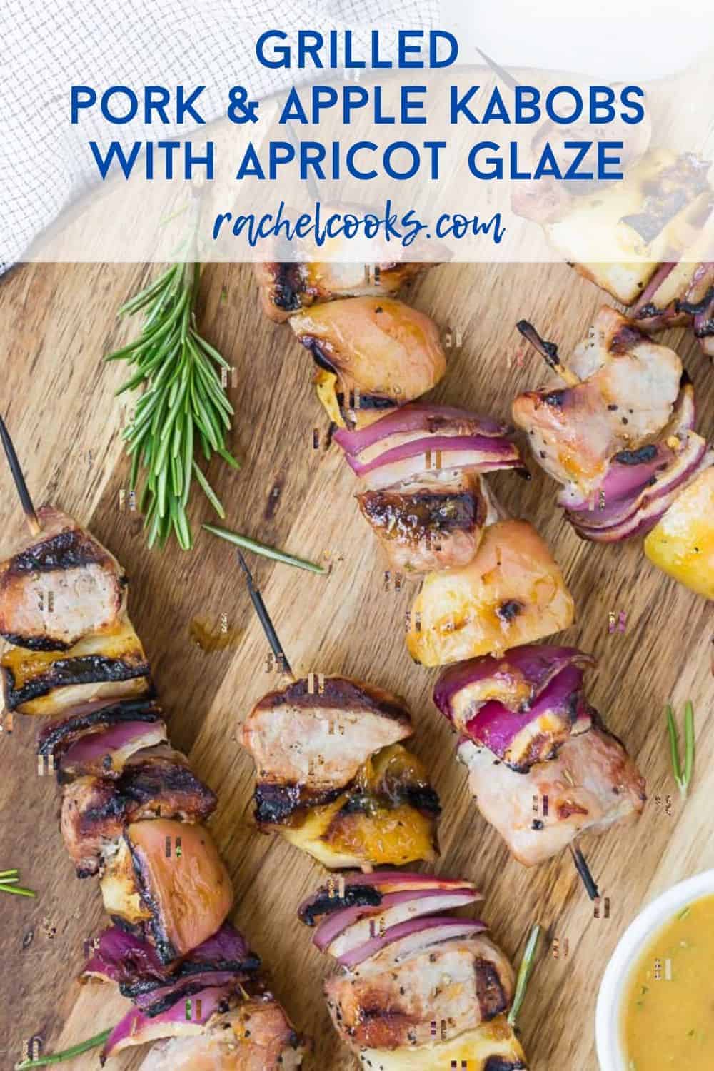 Kabobs of pork chunks, apples, and onions sit on a wooden cutting board. A light orange dipping sauce is in a white bowl next to them. Text overlay reads, "grilled pork & apple kabobs with apricot glaze."