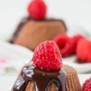 Small chocolate cheesecakes topped with chocolate syrup and raspberries.