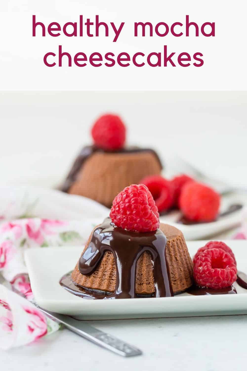 Small chocolate cheesecakes topped with chocolate syrup and raspberries.