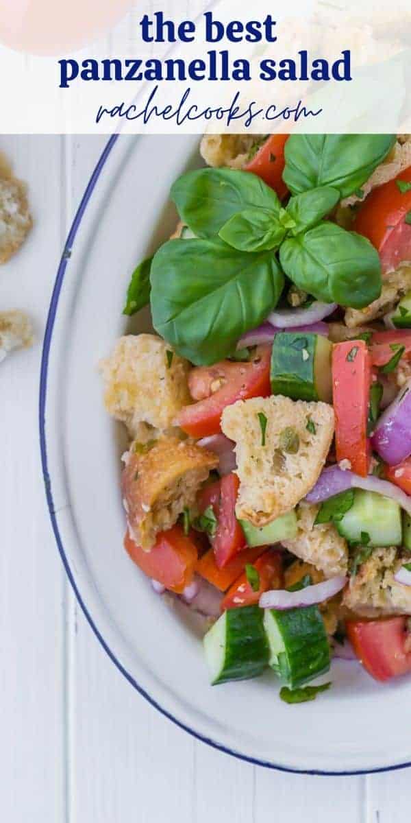 Salad on a white plate, consisting of tomatoes, cucumbers, croutons, fresh herbs, and red onions. Text overlay reads "How to Make Panzanella."