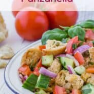 Salad on a white plate, consisting of tomatoes, cucumbers, croutons, fresh herbs, and red onions. Text overlay reads "How to Make Panzanella."