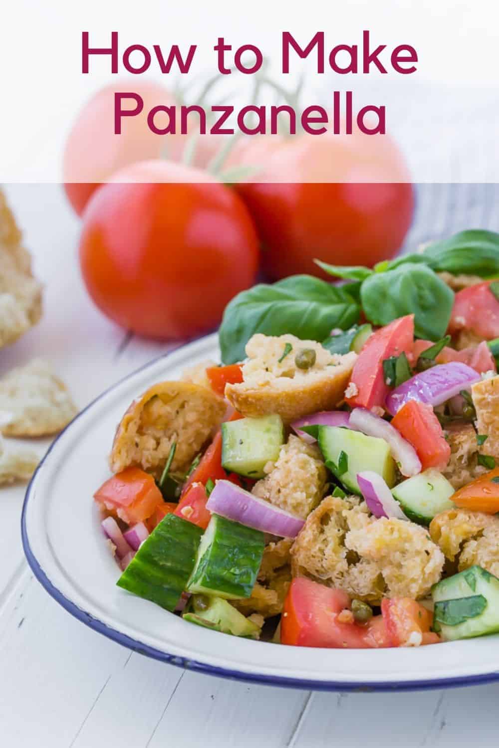 Salad on a white plate, consisting of tomatoes, cucumbers, croutons, fresh herbs, and red onions. Text overlay reads "How to Make Panzanella."