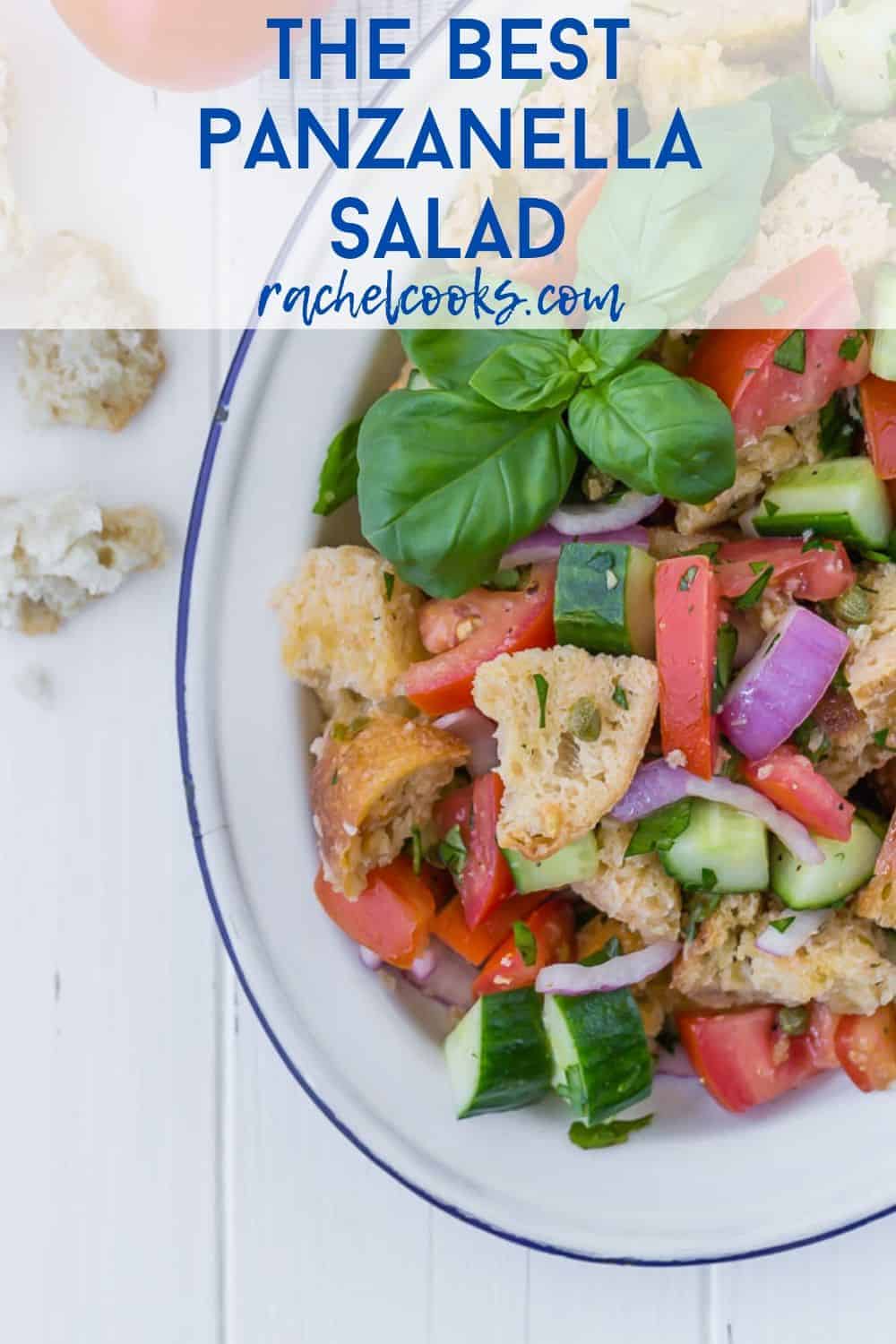 Salad on a white plate, consisting of tomatoes, cucumbers, croutons, fresh herbs, and red onions. Text overlay reads "the best panzanella salad - rachelcooks.com"