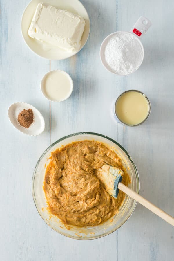 Pumpkin poke cake batter in a bowl next to more ingredients on a countertop.