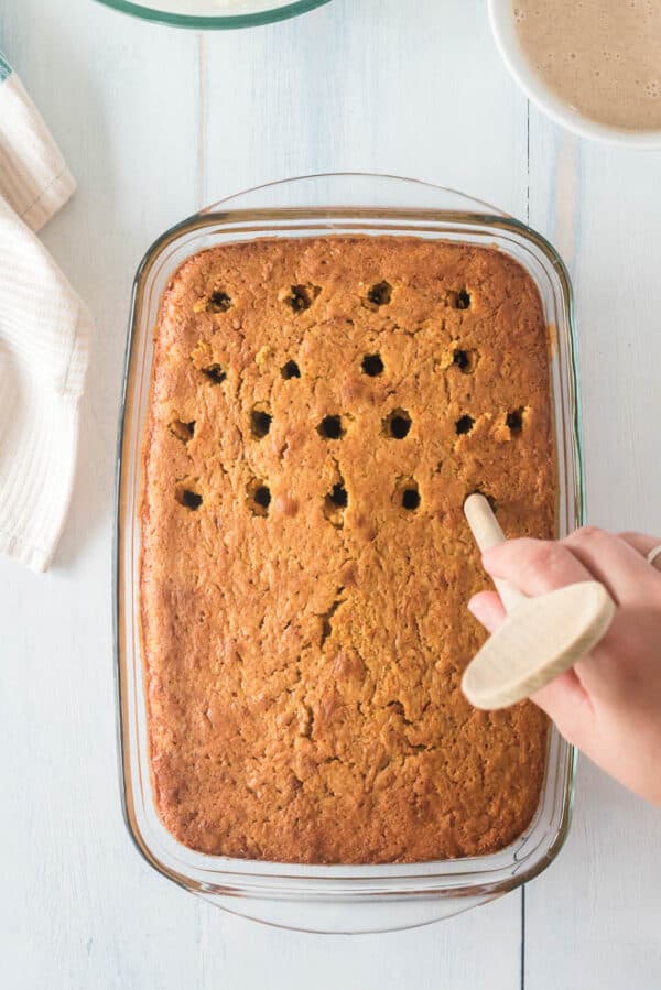 Holes being poked in a baked pumpkin cake with a wooden spoon handle.