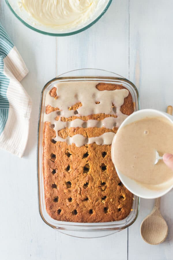 Sweetened condensed milk seasoned with cinnamon being drizzled over a poke cake.