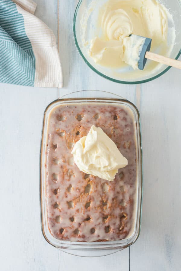 A dollop of cream cheese frosting on top of a pumpkin poke cake.