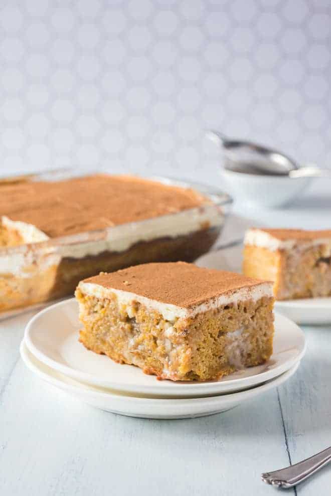 Pumpkin poke cake on a white plate, more cake in the background.