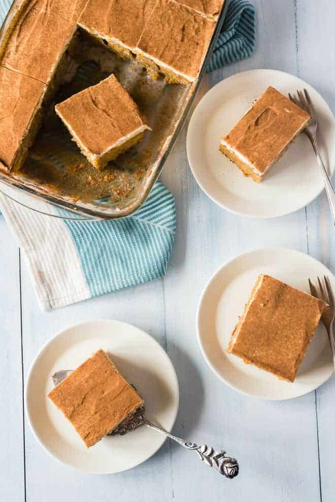 Overhead view of multiple slices of pumpkin poke cake served on plates next to the rest of the cake in a pan.
